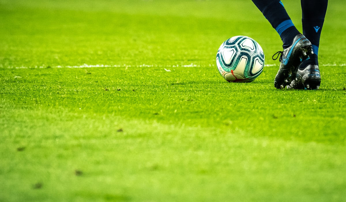 緑の芝生の上でボールを扱うサッカー選手の足元