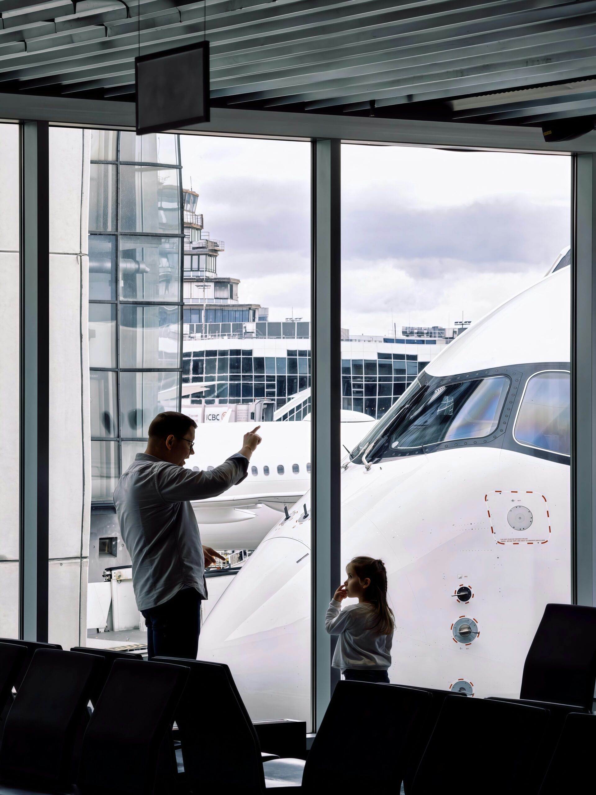 空港の窓越しに飛行機を見る父親と子ども